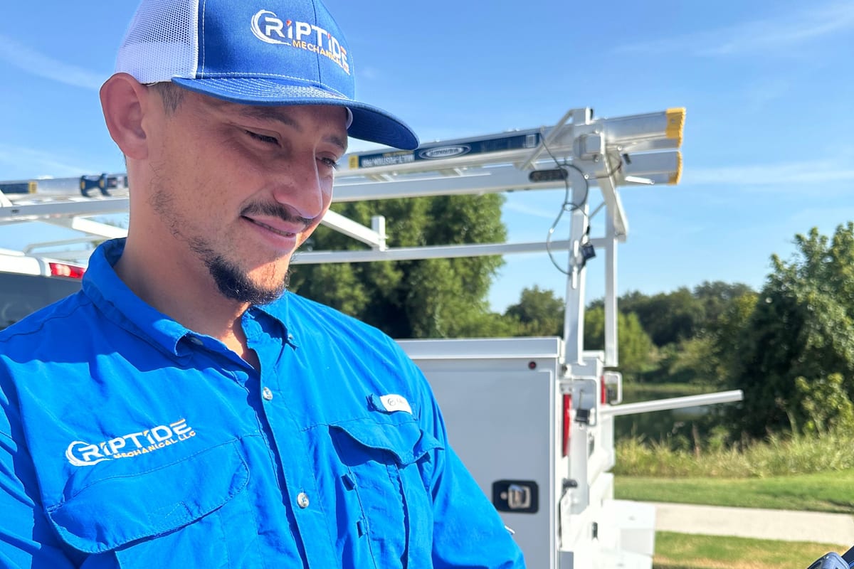 A Riptide Mechanical technician holding a tablet showing the Riptide Family Circle membership benefits, service truck behind him