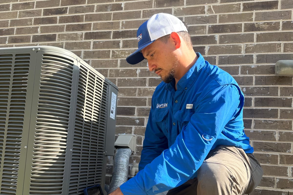 A Riptide Mechanical technician kneeling at an outdoor condenser during a service visit
