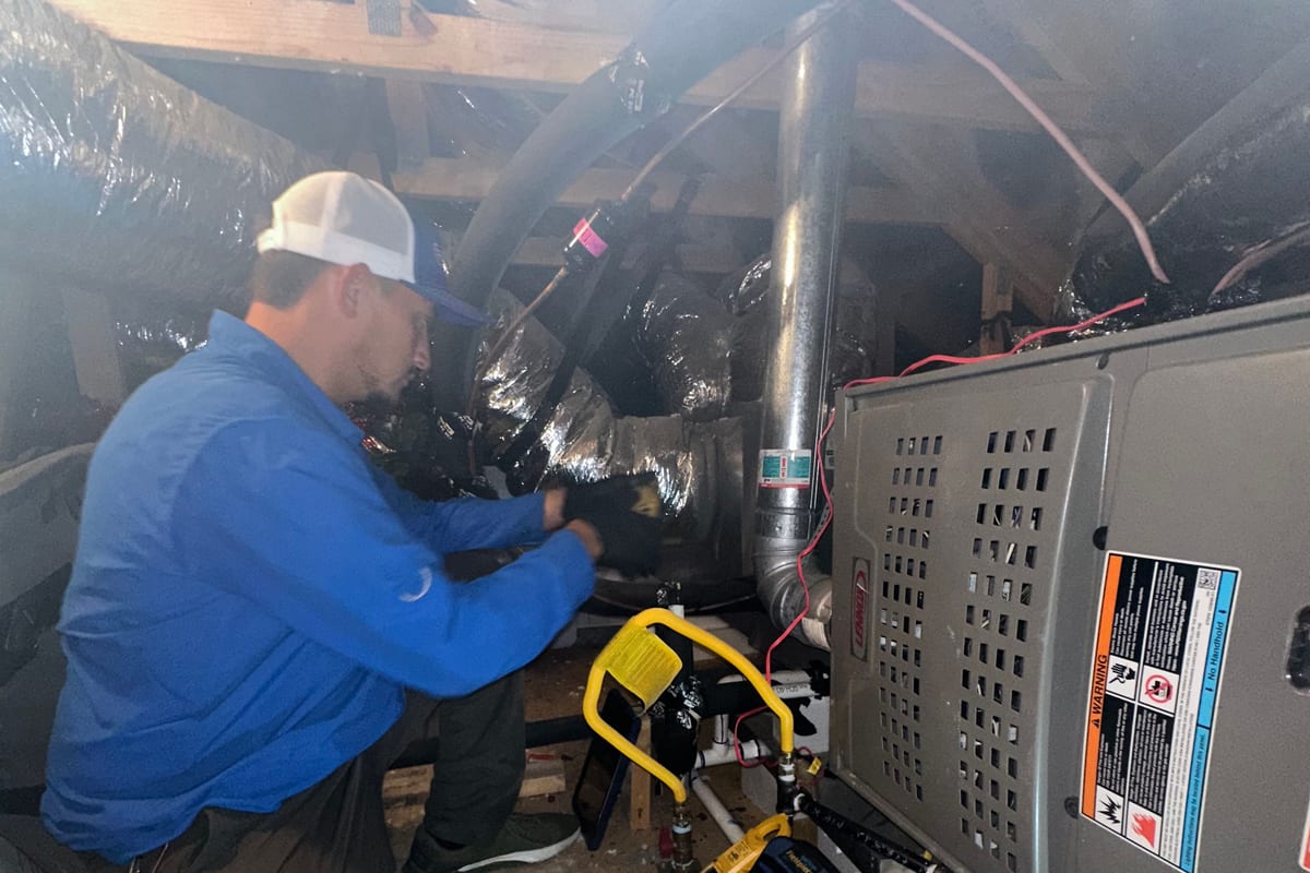 A Riptide Mechanical technician working on a gas furnace with gauges and a work light