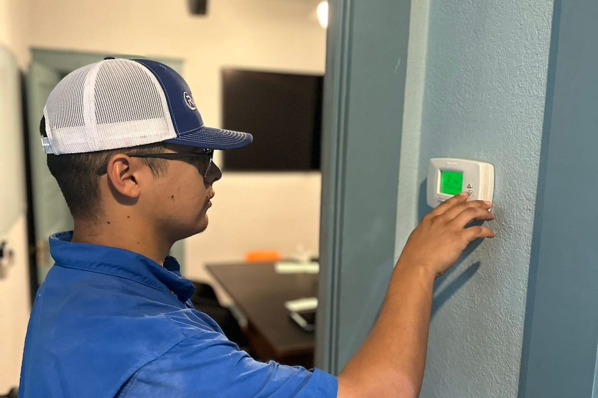 A Riptide Mechanical technician checking a wall thermostat inside a home